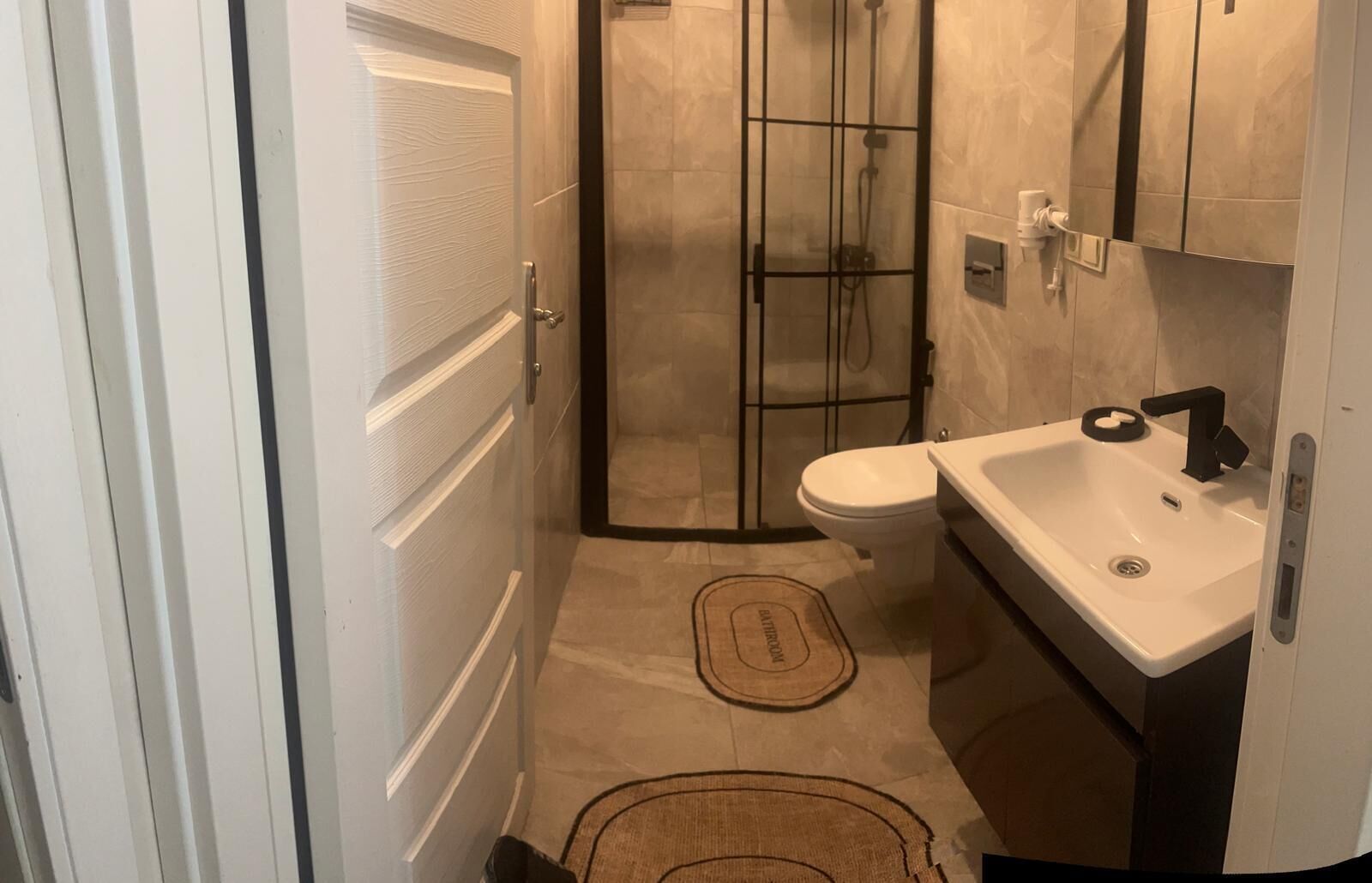 A bathroom with a glass shower enclosure, a toilet, and a sink with a black faucet.