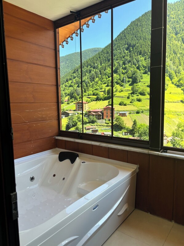 Un baño con una bañera grande y vistas a un valle verde a través de una ventana.
