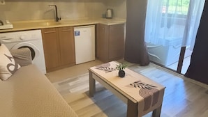 A compact living space with a kitchenette, a sofa, a coffee table, and a view of greenery through large windows. - Uzungöl Ozturk Hotel  (Çaykara)