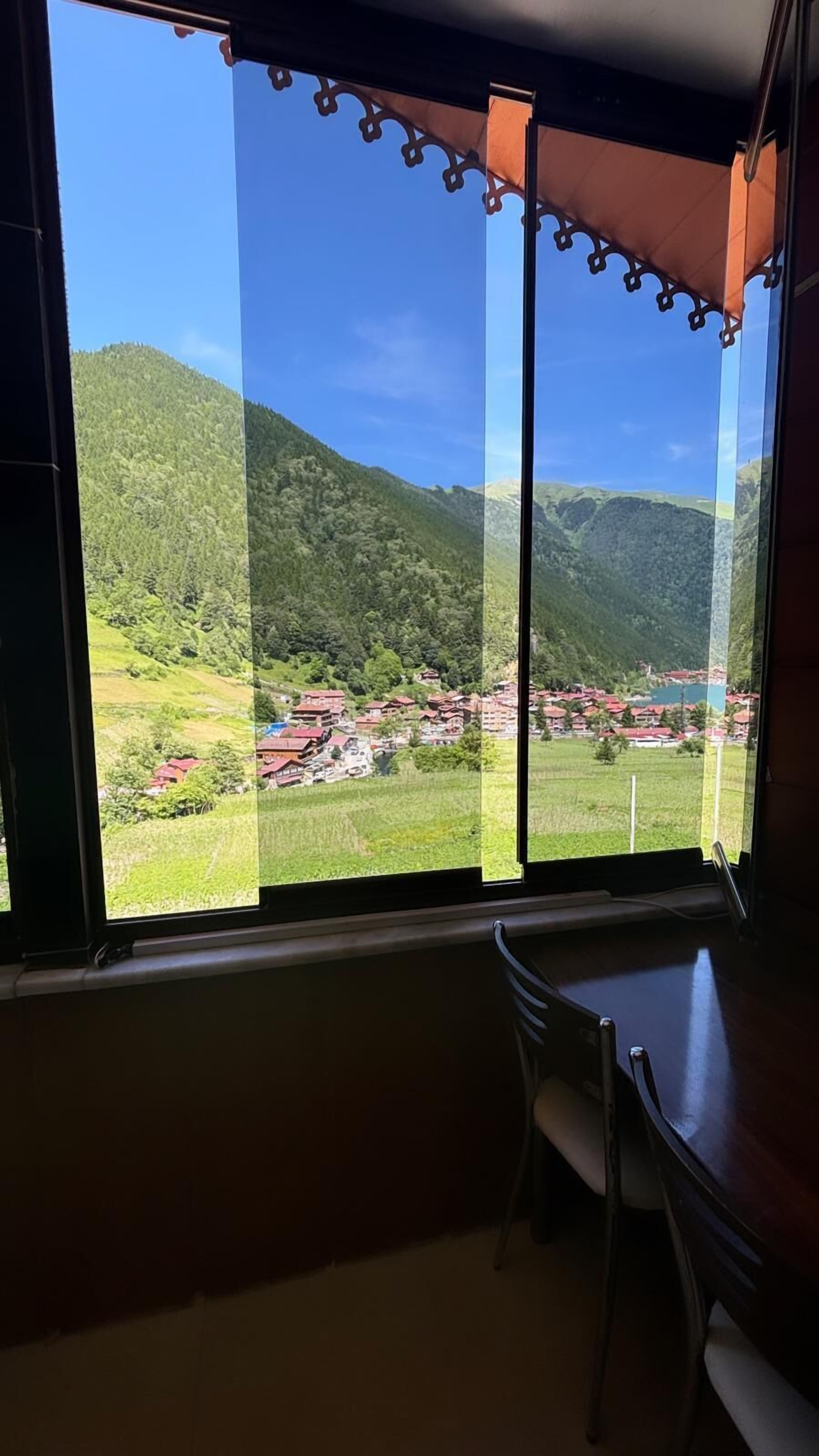 A room with a large window overlooking a mountainous landscape with a village below.
