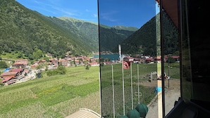 A view from a window overlooking a village with houses and a lake, with mountains in the background. - Uzungöl Ozturk Hotel  (Çaykara)