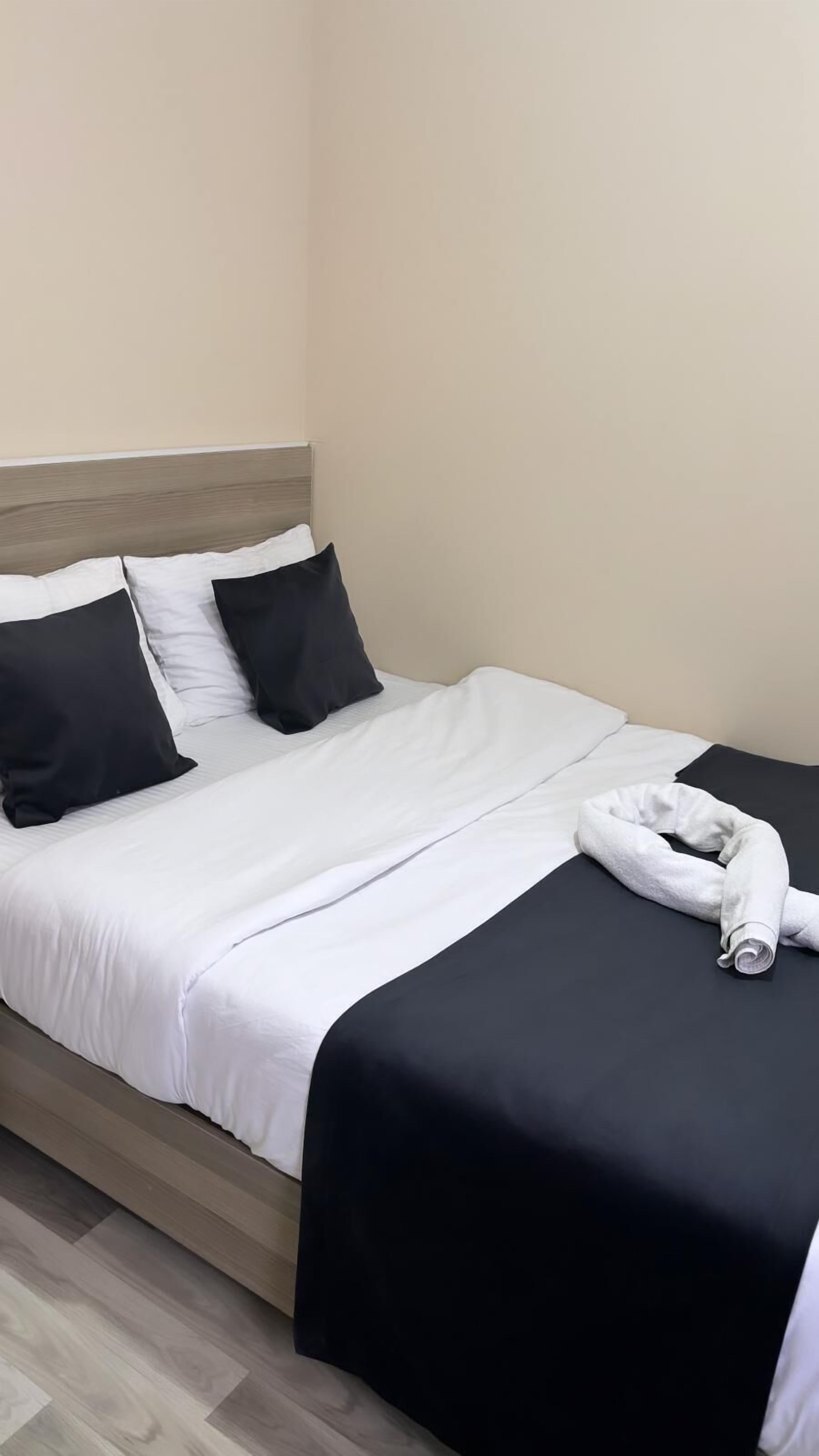 A neatly made bed with white and black bedding, a wooden headboard, and a rolled towel on the bed.
