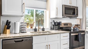 A modern kitchen with white cabinetry, a stainless steel dishwasher, a built-in oven, a microwave, and a coffee maker.