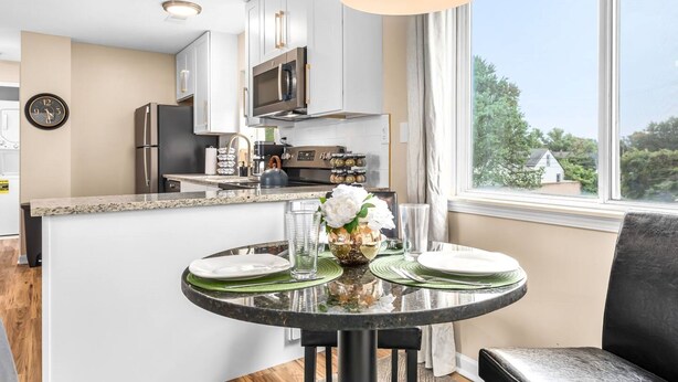 A modern kitchen with white cabinets, stainless steel appliances, and a dining area with a round table and chairs.