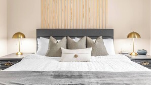 A neatly made bed with a grey headboard, two bedside tables with lamps, and a wooden slat wall behind the bed.