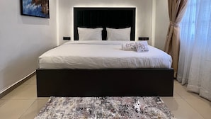 Une chambre à coucher moderne avec un grand lit, une tête de lit, un tableau au mur et un tapis à motifs.
