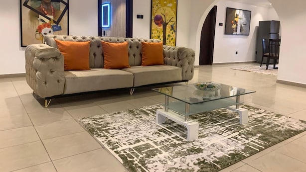 Un salon moderne avec un canapé capitonné, une table basse en verre et des œuvres d’art abstraites accrochées au mur.