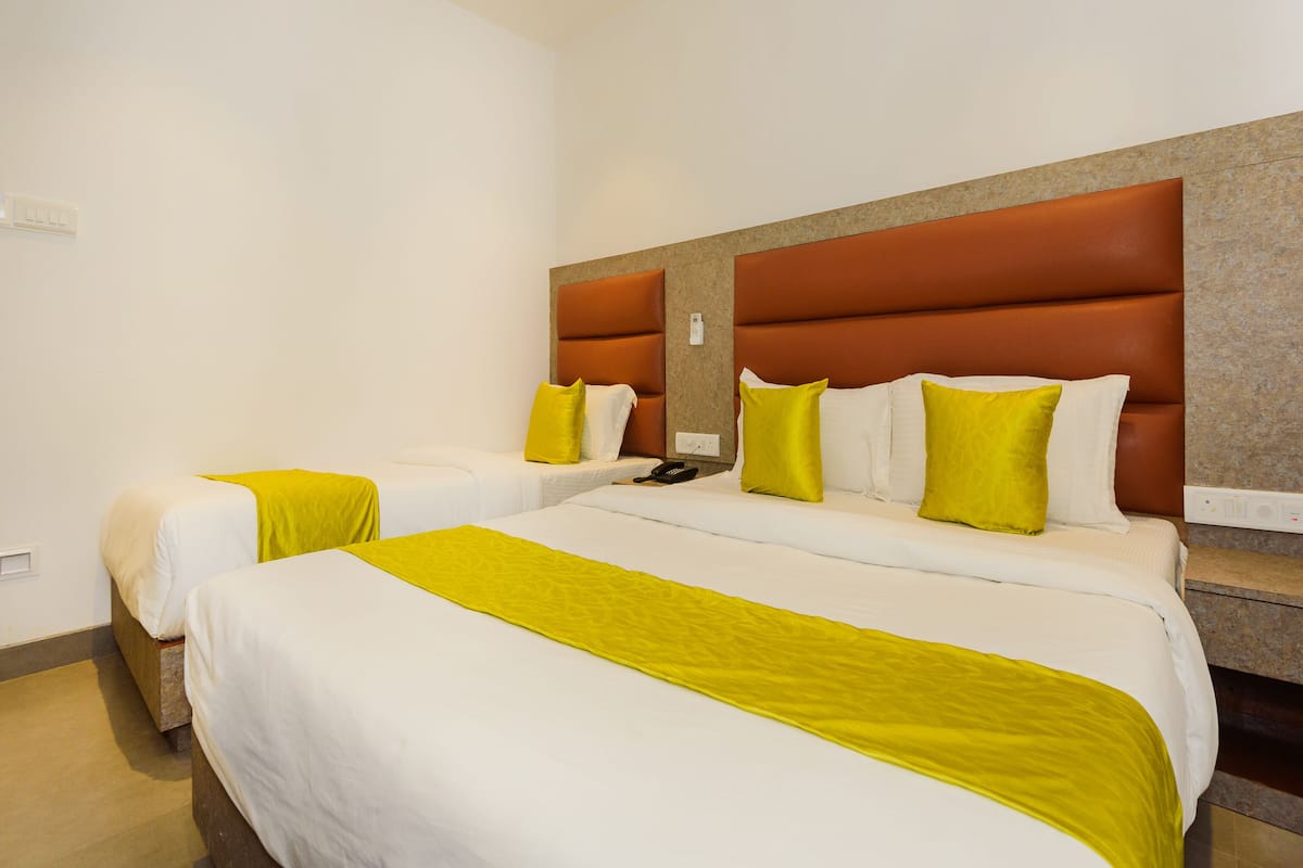 A hotel room with two beds, each with white bedding and yellow accents, a brown headboard, and a small bedside table.