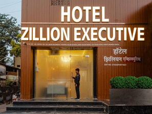 L’extérieur du Zillion Executive Hotel présente un design moderne, avec une grande enseigne et un agent de sécurité posté devant l’entrée.