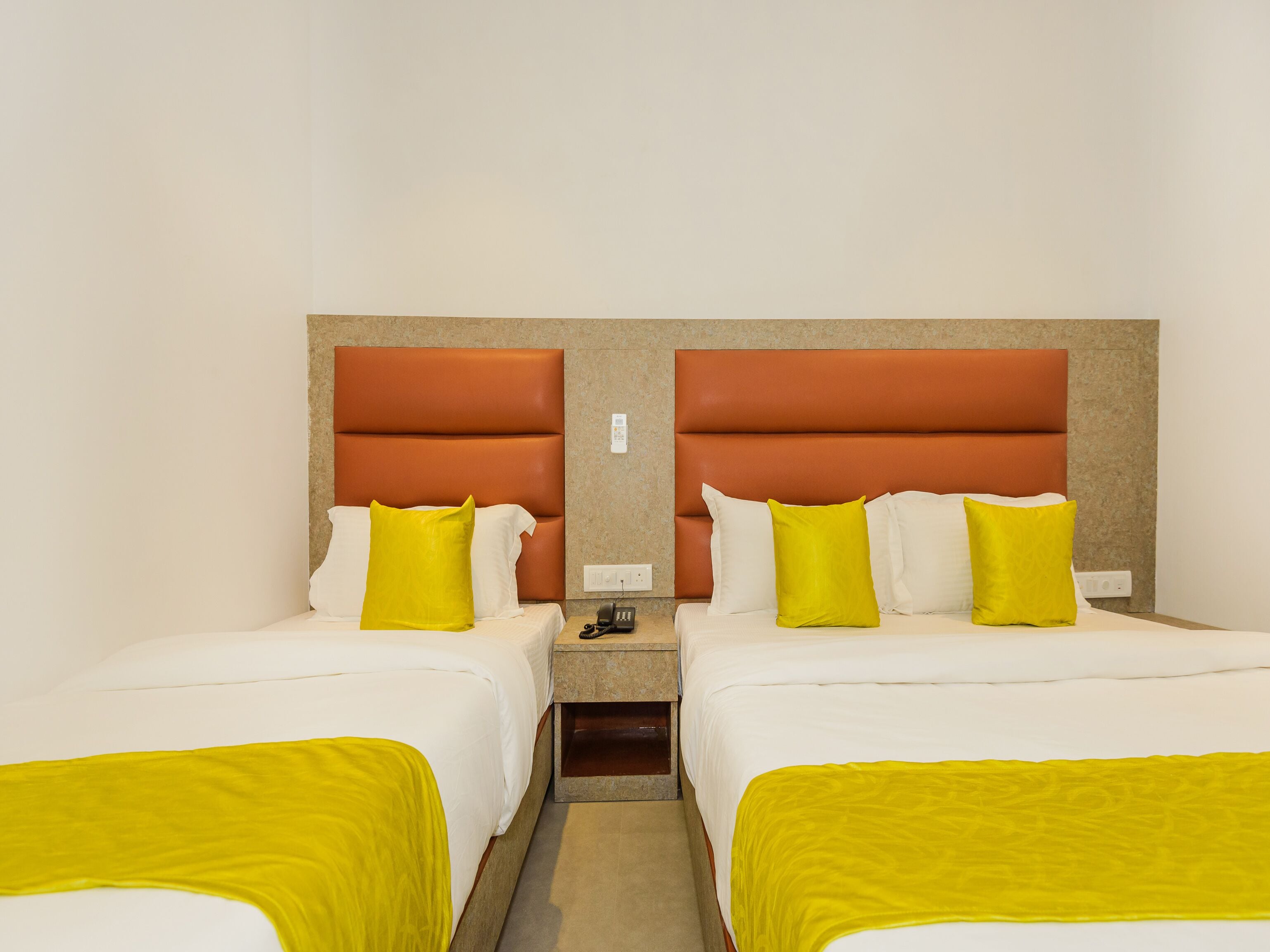 A hotel room with two beds, each with a headboard, and a nightstand between them.