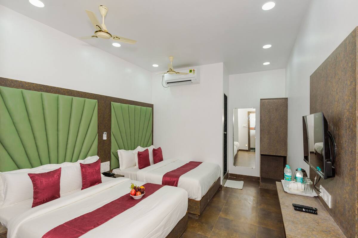 A hotel room with two beds, a TV, and an air conditioning unit.