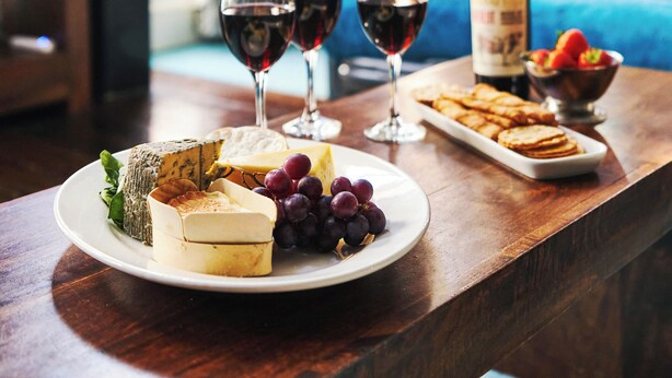 A dining table with a plate of cheese, grapes, crackers, and a bottle of wine.