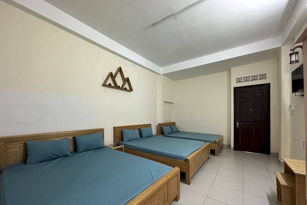 A hotel room with three wooden beds, a tiled floor, a wooden bench, and a door with a decorative sign above it.