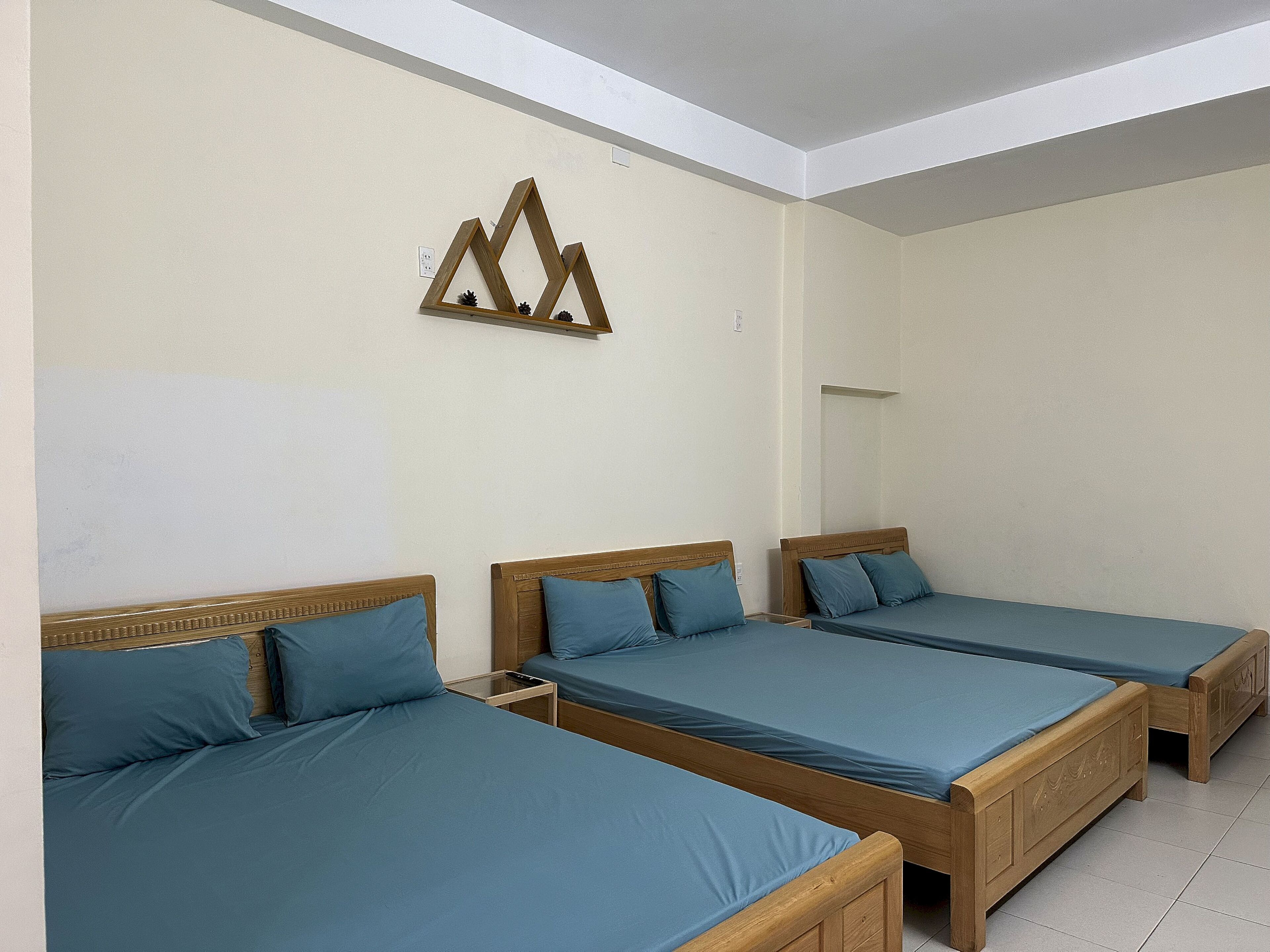 A hotel room with three wooden beds, each with a blue mattress and matching pillows.