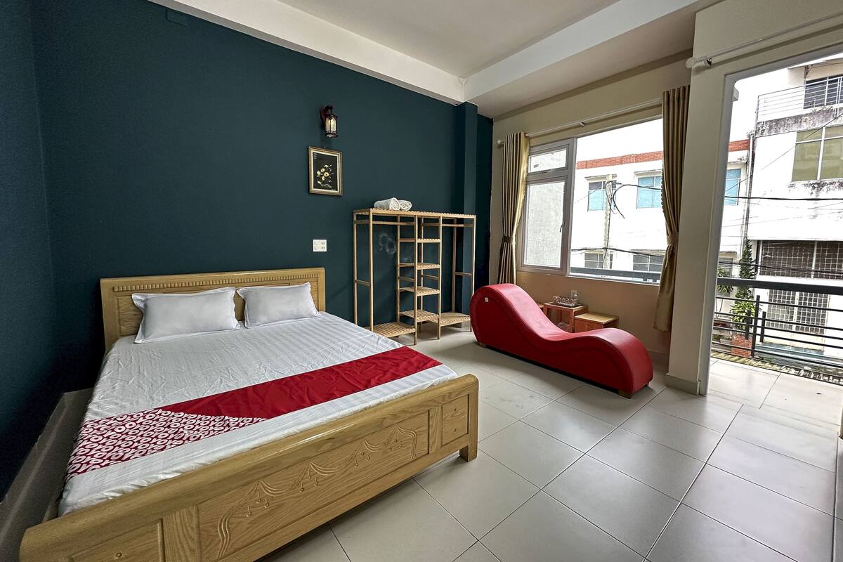 A bedroom with a wooden bed, a red chair, a small table, and a window with a view of buildings.