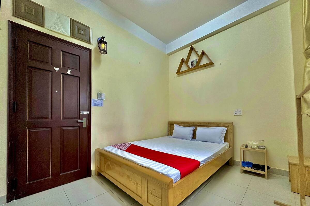 A bedroom with a wooden bed, a door, a wall-mounted light, and a shelf with shoes.