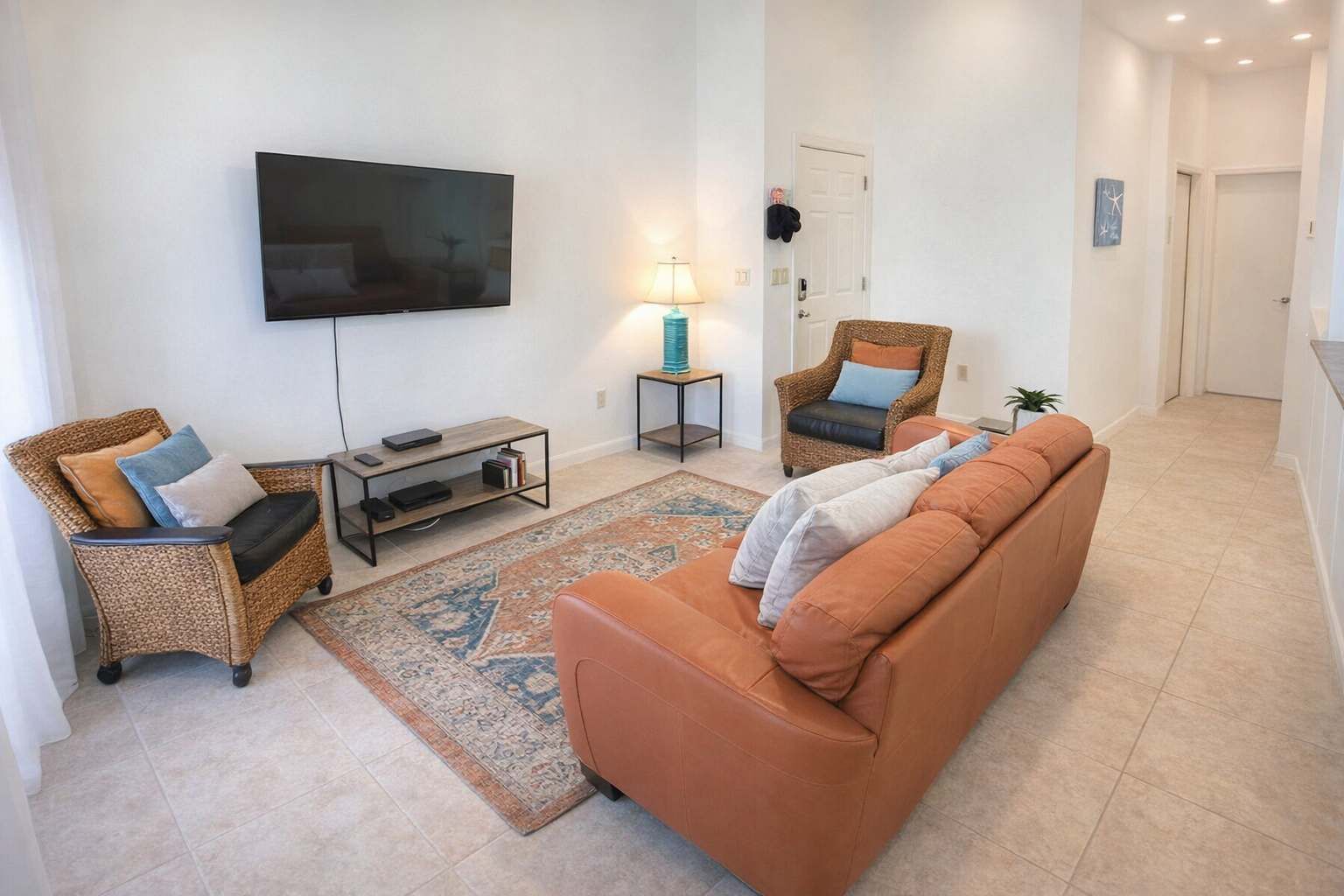 A living room with a flat-screen TV, two wicker chairs, a brown sofa, a small table, and a patterned rug.