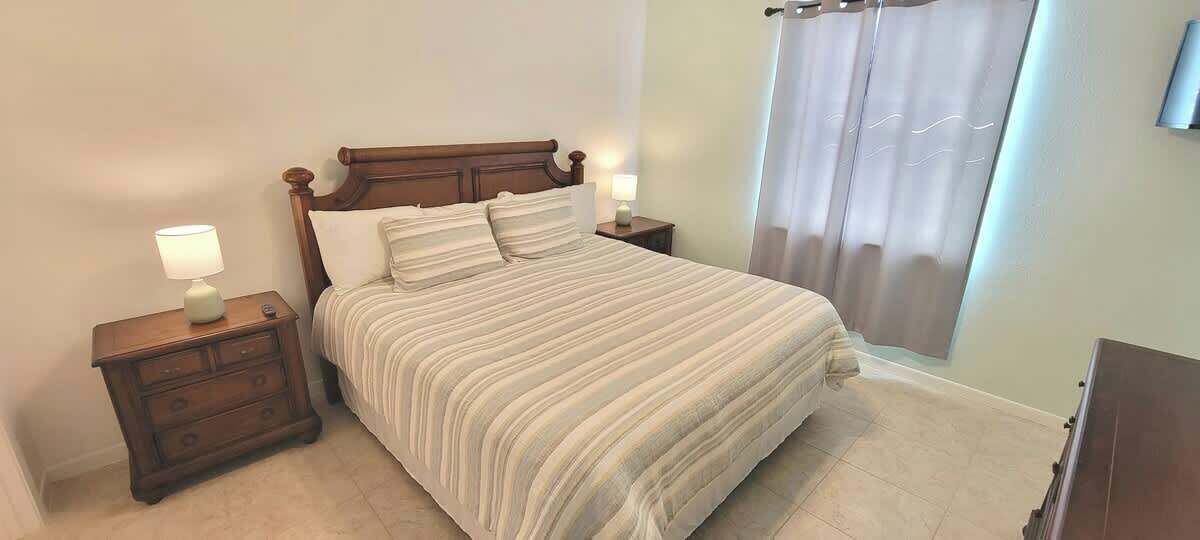A bedroom with a large bed, two bedside tables, a nightstand, and a window with curtains.
