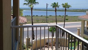 A balcony with a view of a swimming pool, palm trees, and a body of water. - Pool - Beach Access - Near Claytons Private (South Padre Island)