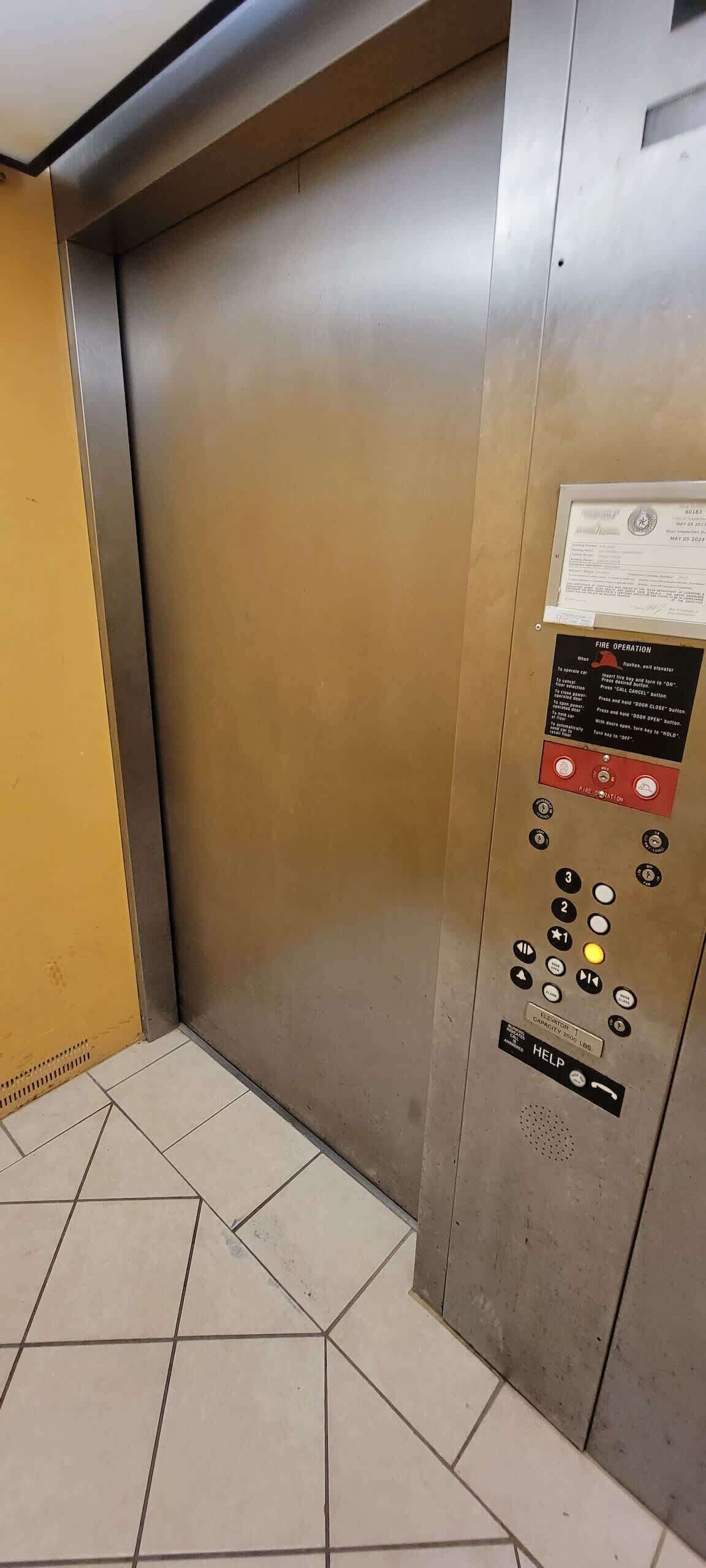 An elevator with a fire operation panel, emergency instructions, and a capacity limit sign.