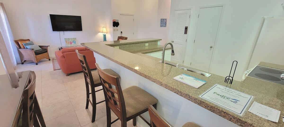 Een moderne keuken met een granieten aanrecht, een inbouwspoelbak en een eethoek met een rode bank en twee barkrukken.
