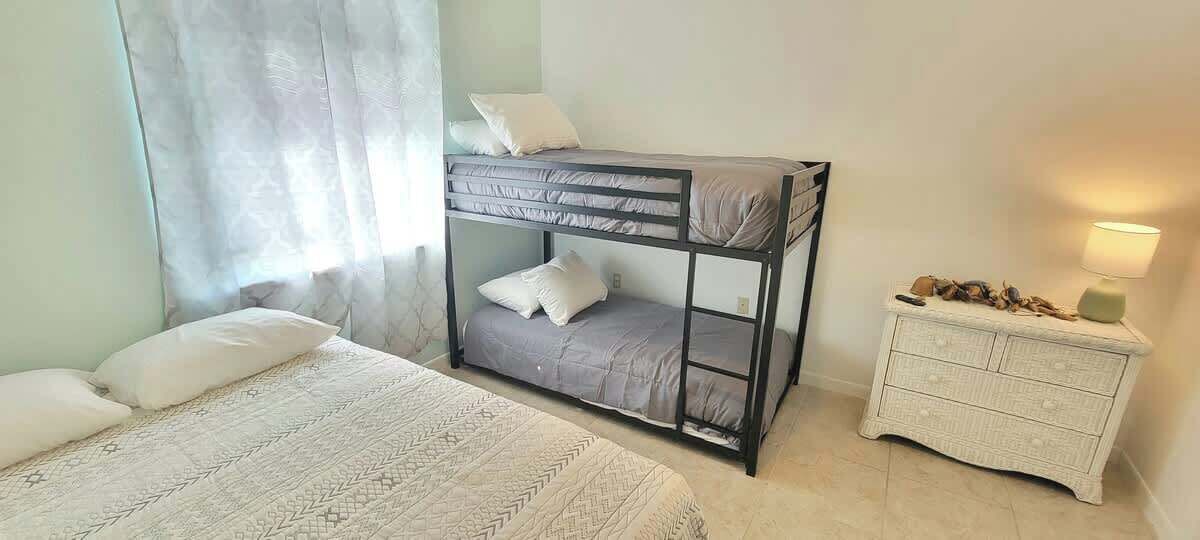 A bunk bed with a lower bunk, a white bedside table with drawers, and a lamp.