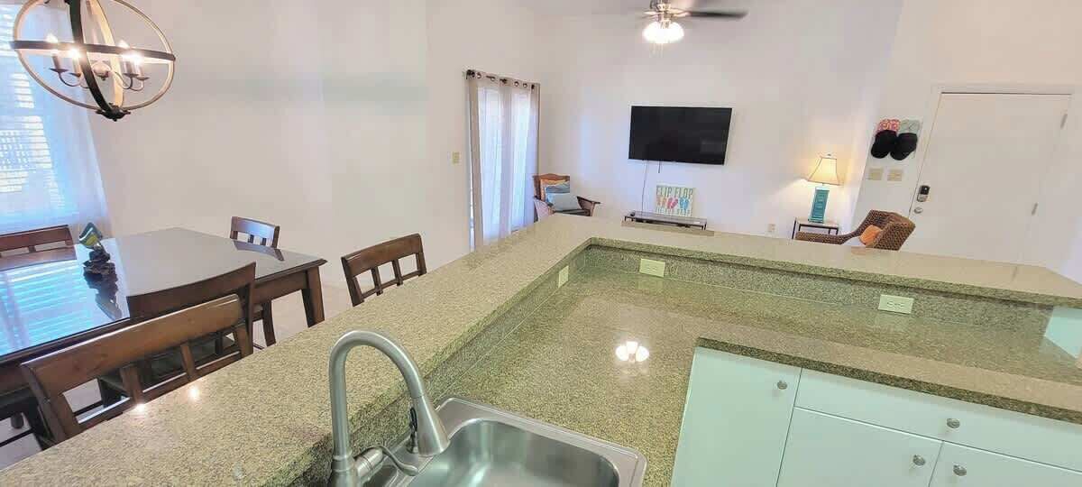 A kitchen with a granite countertop, stainless steel sink, and a dining area with a table and chairs.