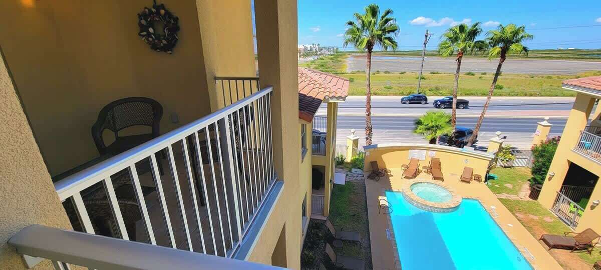 A balcony with a view of a swimming pool, palm trees, and a road with cars.
