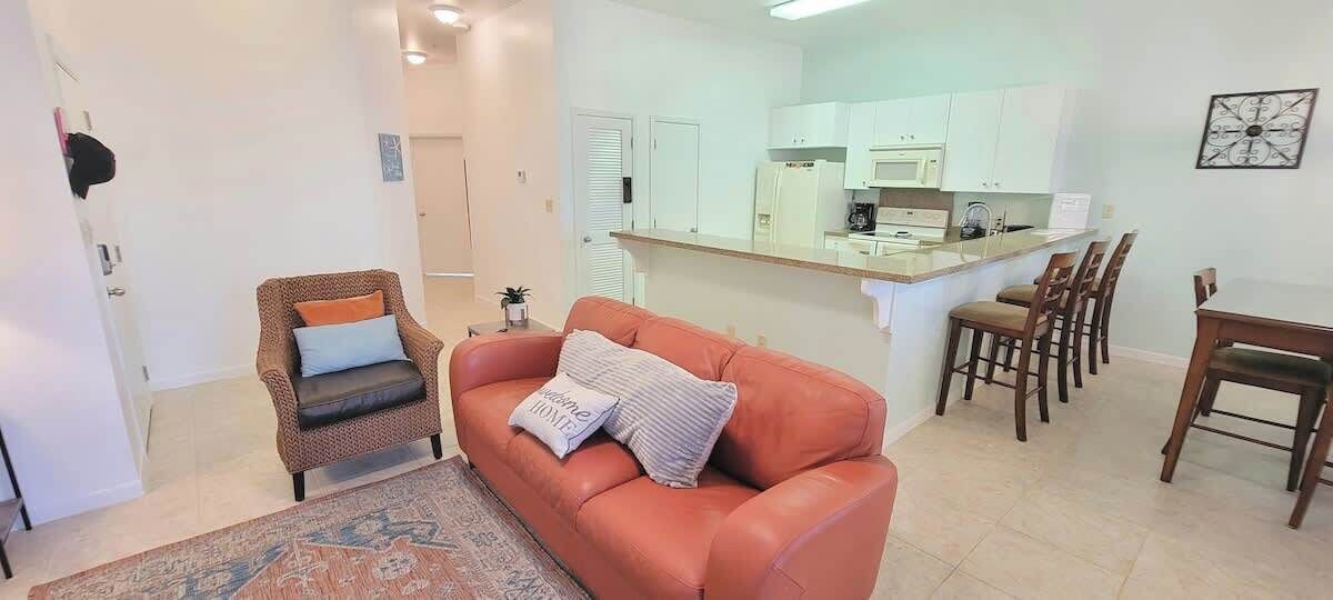 Un salon comprenant un canapé, un fauteuil, un tapis et un coin repas avec des chaises et une table.