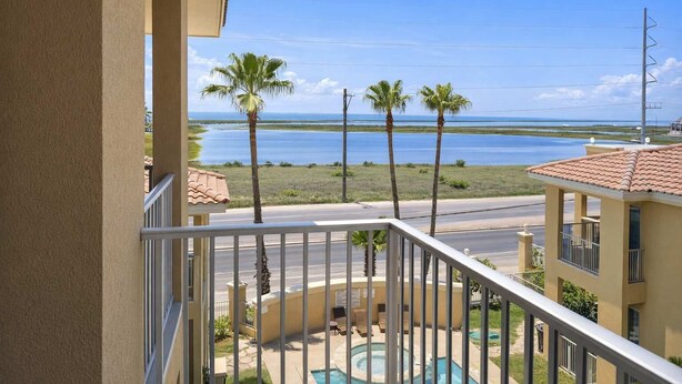 A balcony with a view of a swimming pool, palm trees, and a body of water. - Pool - Beach Access - Near Claytons Private (South Padre Island)