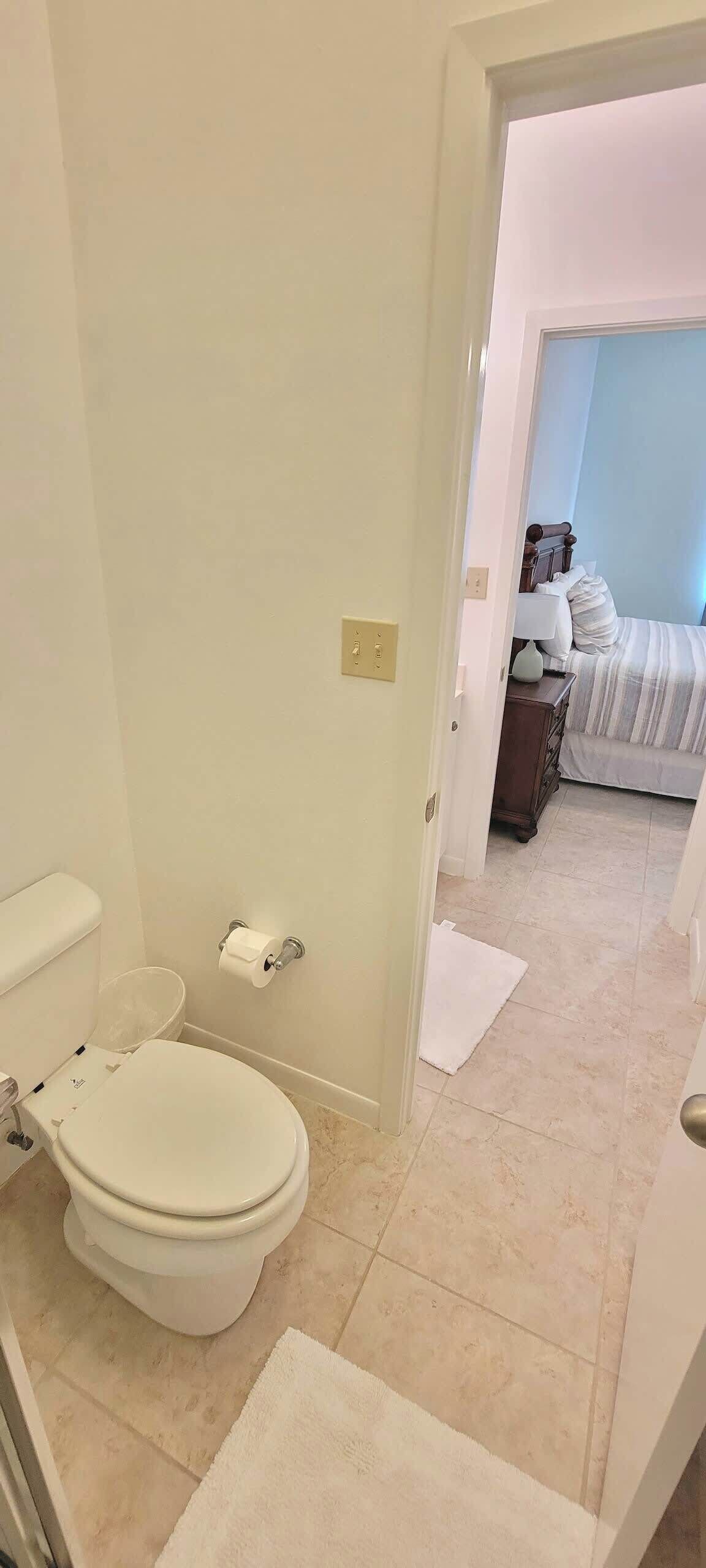 Une salle de bain avec des toilettes, une serviette et une porte visible donnant sur une chambre.