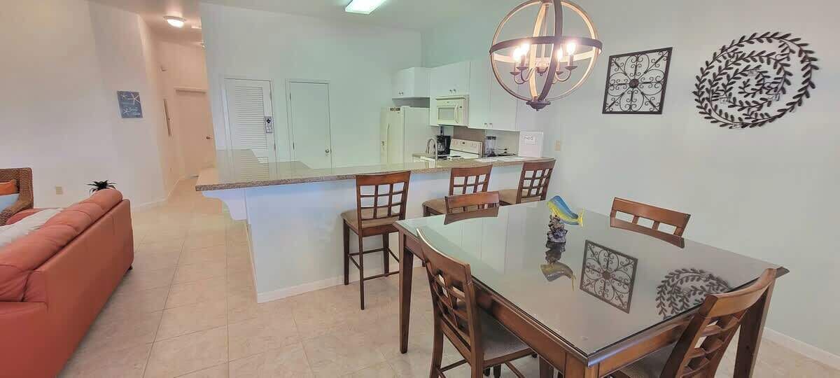 Cozinha moderna com armários brancos, uma ilha central com cadeiras e uma mesa de jantar.