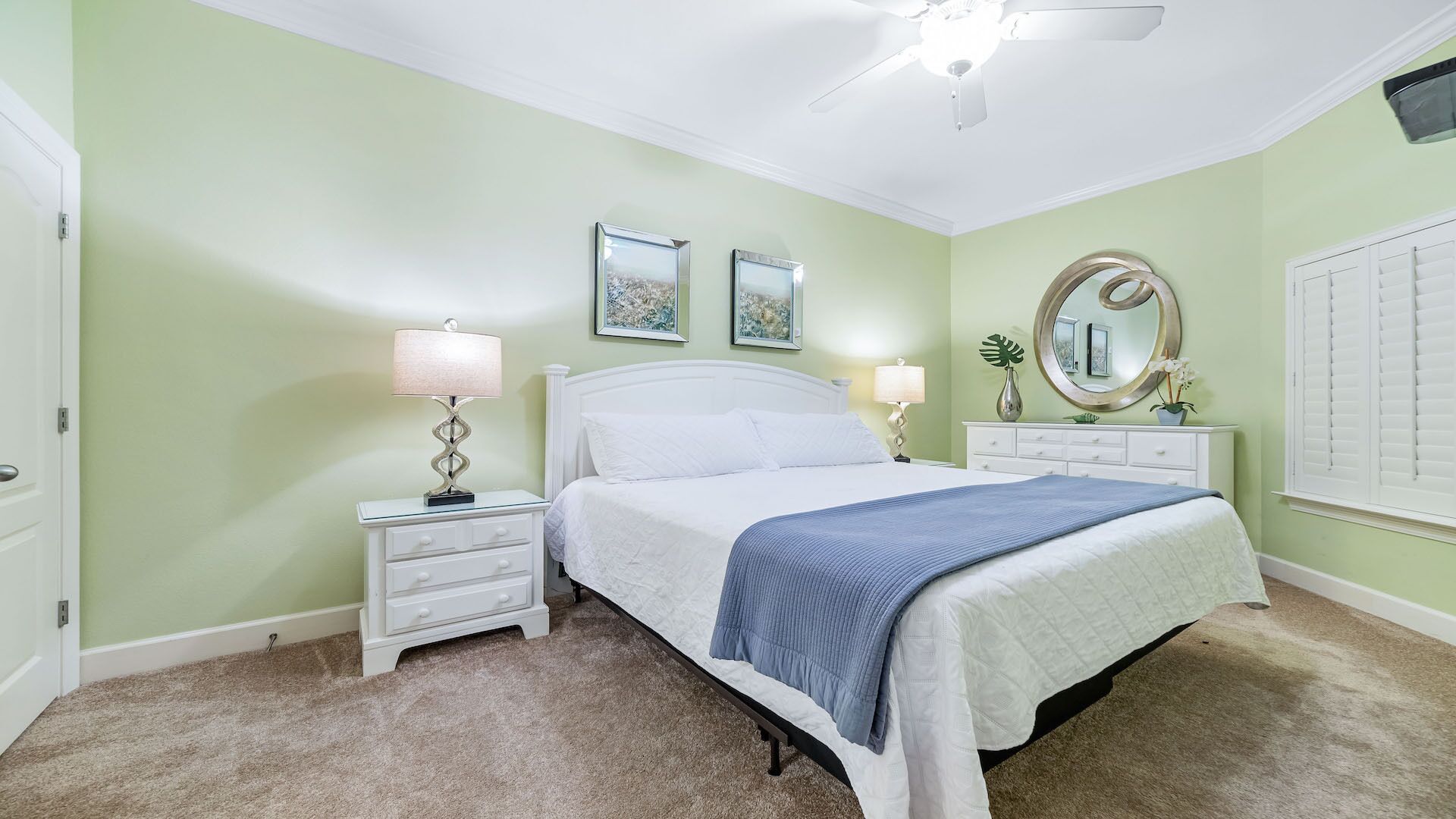 A bedroom with a bed, two bedside tables, a ceiling fan, and two wall-mounted paintings.