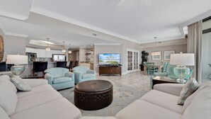 A spacious living room with a large sofa, two armchairs, a coffee table, and a television. There is a dining area with a table and chairs, and a kitchen in the background. - 3rd Floor!! Parking Level!  Avoid the Elevators!! (Orange Beach)
