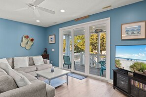 Un salon comprenant un canapé, une table basse et un téléviseur. Une porte-fenêtre coulissante donne accès à une terrasse aménagée avec du mobilier d’extérieur.