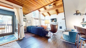 Un salon spacieux avec un plafond en bois, un grand canapé, une table basse et un téléviseur fixé au mur.