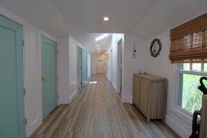 Un couloir doté d’un plancher en bois, de portes de couleur turquoise et d’une fenêtre avec des stores.