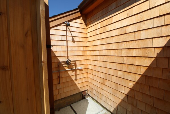 A corner of a wooden building with a metal pipe and a white object mounted on the wall.