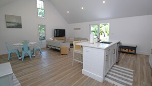 Zona d'estar àmplia amb menjador, sofà, televisió i zona de cuina amb rentatge i armaris.