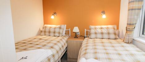 A twin room with two beds, each with a plaid duvet, a bedside table with a lamp, and a wall-mounted light fixture.