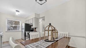 A dining area with a wooden table, white chairs, a striped table runner, and a candle holder. - Southern Comfort Cottage in the City (Lansing)