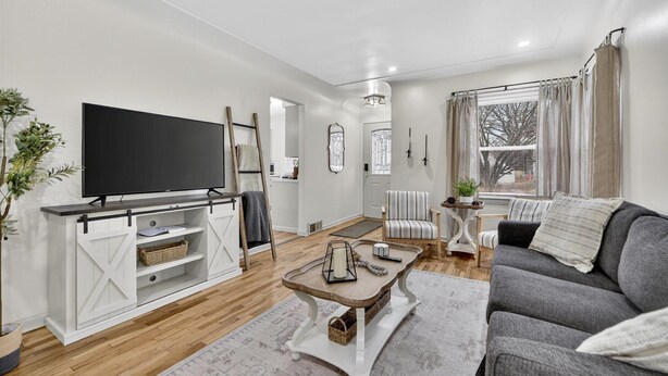 A modern living room with a flat-screen TV, a sofa, a coffee table, and a dining area with a table and chairs. - Southern Comfort Cottage in the City (Lansing)