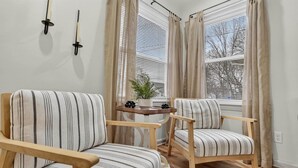 A room with two striped armchairs, a small table with a plant, and a window with blinds. - Southern Comfort Cottage in the City (Lansing)