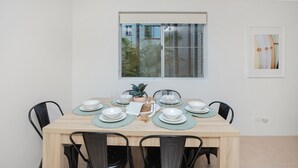 A dining area with a wooden table set for six, black chairs, and a window with a view of buildings and trees. - Breezy, Stylish, Getaway (Tuncurry)