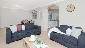 A modern living room with two grey sofas, a wooden coffee table, and a kitchen in the background. - Breezy, Stylish, Getaway (Tuncurry)