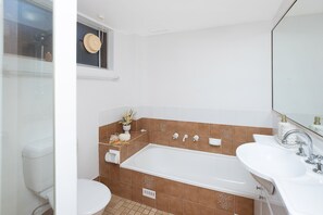 A modern bathroom with a bathtub, two sinks, and a window with a decorative item. - Breezy, Stylish, Getaway (Tuncurry)