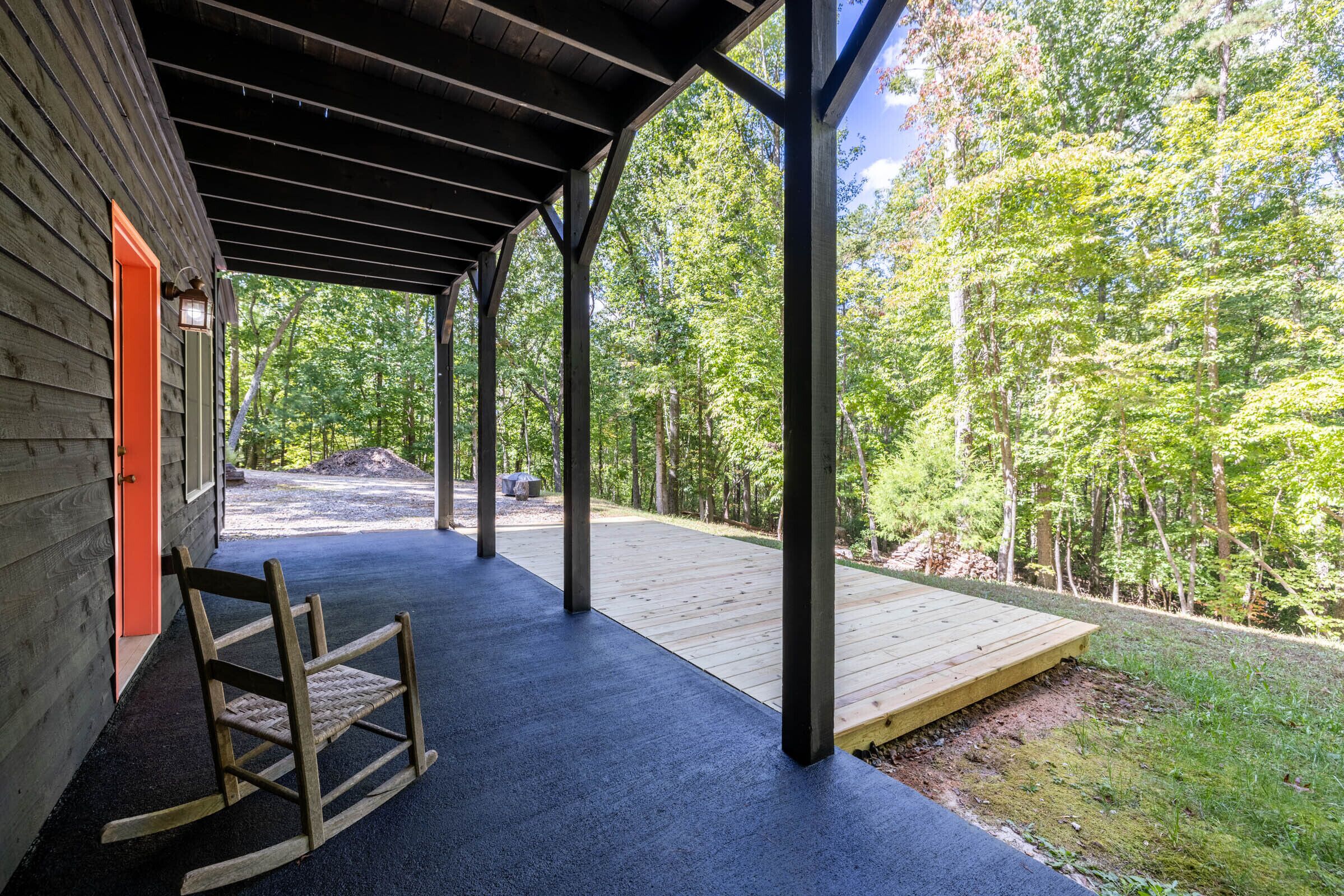 Un espacio al aire libre techado con una terraza de madera, una mecedora y vistas a un área boscosa.