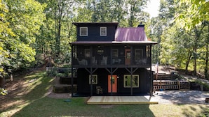 A two-story cabin with a balcony, surrounded by a forest. - Black Bear Bungalow - Lovely Chalet in the Woods (Clarkesville)