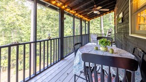 A wooden deck with a table and chairs, surrounded by a railing, overlooking a forested area. - Black Bear Bungalow - Lovely Chalet in the Woods (Clarkesville)