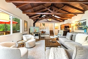 A spacious living room with a high ceiling, a television, comfortable seating, and artwork on the walls.